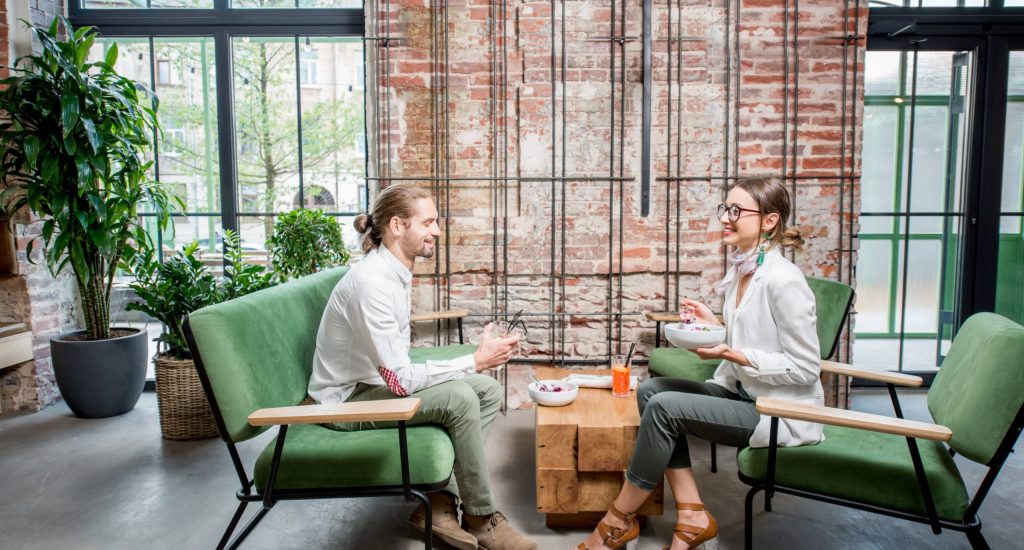 Business people sitting on the green sofas during a lunch at the beautiful loft interior on the brick wall background